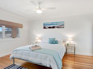 a white bedroom with a bed with a ceiling fan at Sienna by the Sea in Callala Beach