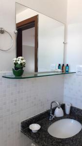 a bathroom sink with a mirror and a vase of flowers at Loft tropical na praia de Vilas do Atlântico in Lauro de Freitas