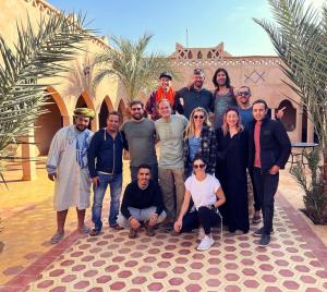 eine Gruppe von Personen, die sich vor einem Gebäude für ein Bild ausgeben in der Unterkunft Auberge Les Roches in Merzouga