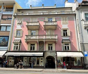 um edifício cor-de-rosa com pessoas a andar à frente dele em Rosa Rooms Meran em Merano