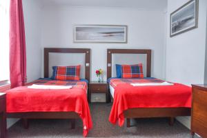 two beds in a room with red sheets and blue pillows at Gatwick Castle B&B in Horley