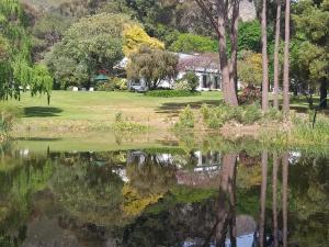 una casa si riflette nell'acqua di un lago di L'Auberge Chanteclair a Franschhoek