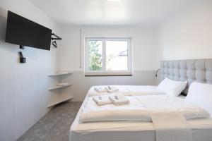 a white bedroom with two beds and a flat screen tv at StayStay Guesthouse I 24 Hours Check-In in Nürnberg