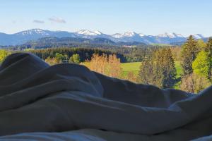 une couverture posée sur un lit avec des montagnes en arrière-plan dans l'établissement Traumhafter Bergblick im Allgäuer Luftkurort, à Buchenberg