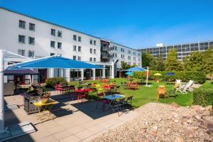 eine Terrasse mit Tischen, Stühlen und blauen Sonnenschirmen in der Unterkunft Greet hotel Darmstadt - an Accor hotel - in Darmstadt