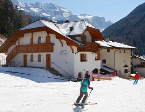 a child on skis in the snow in front of a house at Grohmann Apartments in Selva di Val Gardena