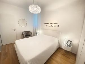 a white bedroom with a bed and a chandelier at Chic In The City in Bolzano