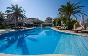 a large swimming pool with chairs and palm trees at Isida Hotel Agia Marina in Agia Marina Nea Kydonias