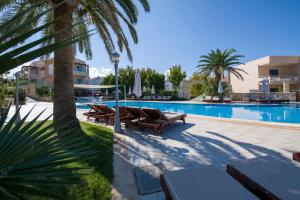 a swimming pool with chaise lounge chairs and a palm tree at Isida Hotel Agia Marina in Agia Marina Nea Kydonias