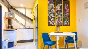 a yellow kitchen with a white table and blue chairs at Carters Beach Seaside Accommodation in Carters Beach