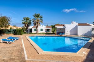 una piscina con sillas azules y una casa en Apartamentos Las Golondrinas, en Cala'n Bosch
