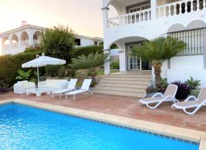 Villa con piscina con sillas y sombrilla en Villa with a big garden and heated pool, en Málaga