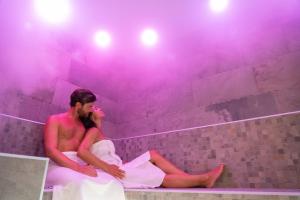 Un uomo e una donna seduti in una vasca da bagno con luci viola di Le Cappuccinelle Suites&SPA a Perugia