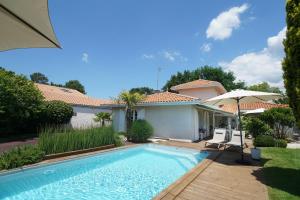 a swimming pool in front of a house with an umbrella at Chambres d'hôtes Villa Surcouf in Andernos-les-Bains