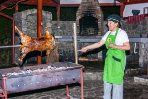 Um homem de avental verde a cozinhar um frango assado. em Pensiunea Boema em Sinaia