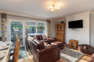 a living room with a leather couch and a television at Hazelglade Cottage - Hot Tub, Games Room, Pet Friendly in Saundersfoot