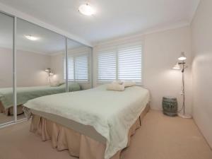a white bedroom with a large bed with mirrors at Kamilaroi, 6/58-60 Magnus Street in Nelson Bay