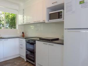 una cucina con mobili bianchi e un forno a microonde di Tamara Court a Sawtell Altre 5 foto