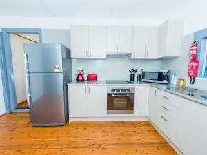 a kitchen with white cabinets and a stainless steel refrigerator at Beach House on James Patterson in Anna Bay