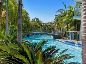 a swimming pool with palm trees and a bridge at Pacific Blue Townhouse, 351/265 Sandy Point Road in Salamander Bay