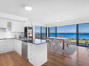 a kitchen with white cabinets and a table with a view of the ocean at Panarea Soldiers Point Road Unit 1 197 in Salamander Bay