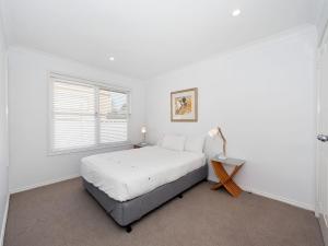 a white bedroom with a bed and a window at Surf Break Unit 10B Tuna Cresent Upstairs in Fingal Bay