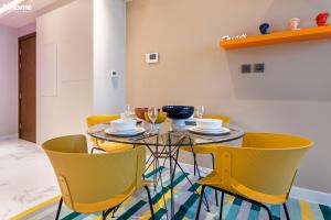 a dining room with a glass table and yellow chairs at bnbmehomes - Lux 2B Apt - Dubai Canal Water View - 4406 in Dubai