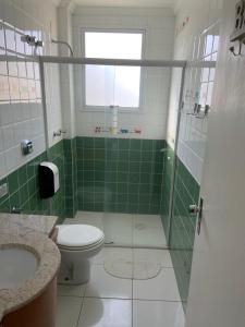 uma casa de banho com azulejos verdes, um WC e um chuveiro em Praia Pousada Tatuíra em Florianópolis