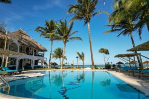 a pool at the resort with palm trees and the ocean at Nest Style Beach Hotel Zanzibar in Makunduchi