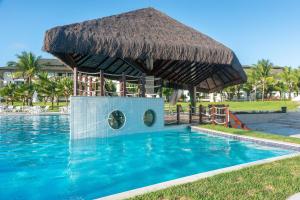 a swimming pool with a straw hut in the middle of it at Flat ou Bangalo Luxo Beach Class Beira Mar Muro Alto in Porto De Galinhas
