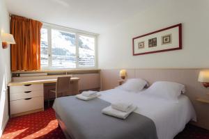 a hotel room with two beds and a desk and a window at Belambra Clubs Les Menuires - Neige Et Ciel in Les Menuires