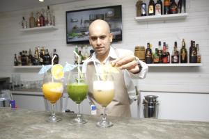 a man standing behind a bar with three cocktails at Hotel Colibrí Suites in Porlamar