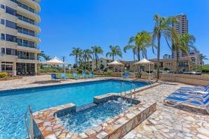 a swimming pool with chairs and a building at Southern Cross Beachfront Holiday Apartments in Gold Coast