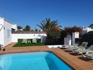 a swimming pool with lounge chairs and a house at FUN FAMILY VILLA-CRAZY GOLF COURSE-HEATED POOL-COCKTAIL BAR-JACUZZI-GAMES ROOM-WIFI &UK TV in Puerto del Carmen