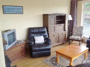 uma sala de estar com uma cadeira de couro preta e uma televisão em Moulamill Cottage em Gouladane