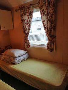 a bed in a room with a window and a pillow at 8 BERTH DELUXE CARAVAN ML88 GOLDEN PALM CHAPEL ST LEONARDs in Chapel Saint Leonards