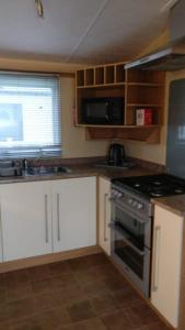 a kitchen with white cabinets and a stove top oven at 8 BERTH DELUXE CARAVAN ML88 GOLDEN PALM CHAPEL ST LEONARDs in Chapel Saint Leonards