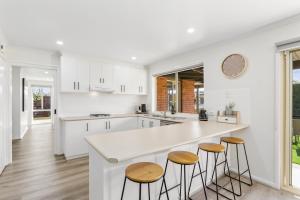 a kitchen with white cabinets and wooden stools at 2 Bedroom Unit - Close To The Beach - Free Parking - Free WIFI in Ocean Grove