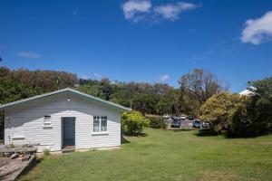 un pequeño edificio blanco con un aparcamiento con coches en Cabana - Original Straddie Beach Shack, en Point Lookout