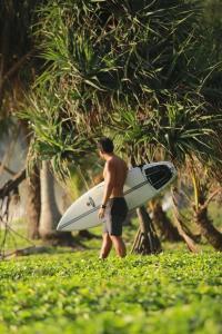 um homem segurando uma prancha de surf na frente de uma árvore em Karon Sea Side em Praia de Karon