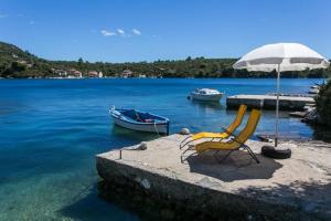 a chair and an umbrella and a boat in the water at Holiday Home Magazin in Slano