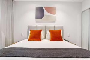 a bedroom with a white bed with orange pillows at Ramada by Wyndham Newmarket Auckland in Auckland