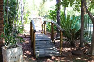 a wooden walkway in a garden with trees and a fence at De la Rose Guesthouse in Lephalale