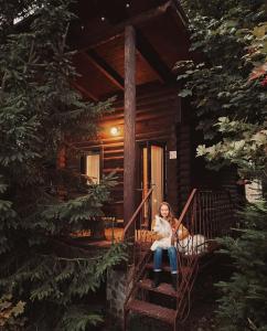 una joven sentada en las escaleras de una cabaña de madera en KLEN Family, en Mykulychyn