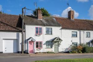 une maison blanche avec une porte rose dans une rue dans l'établissement Luxury 1 bed cottage with hot tub and log burner, à Great Massingham
