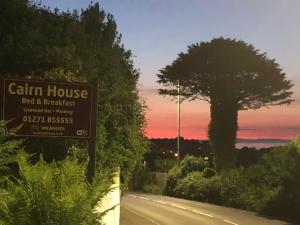 a sign for a farm house on a road with a tree at Cairn House - Bed & Breakfast in Ilfracombe