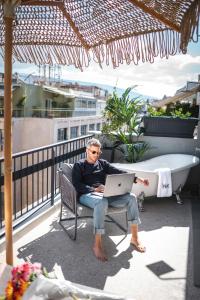 a man sitting in a chair with a laptop on a balcony at PAME House in Athens