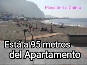 a beach with people sitting on the sand and the ocean at APARTAMENTO en PLAYA CALERA in Valle Gran Rey