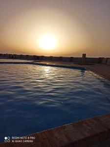 a swimming pool with the sunset in the background at شاليه مرقيا بالساحل الشمالي صف اول بحر in Dawwār ‘Abd al Qādir Qāsim