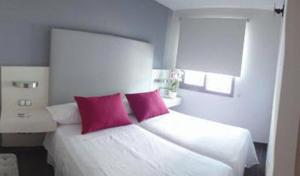 una camera con un letto bianco con due cuscini rosa di Hotel Avenida 31 a Marbella